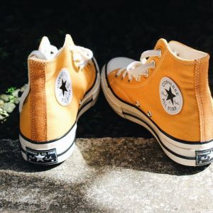Close-up of orange high top sneakers on sunlit concrete, conveying casual fashion vibes.
