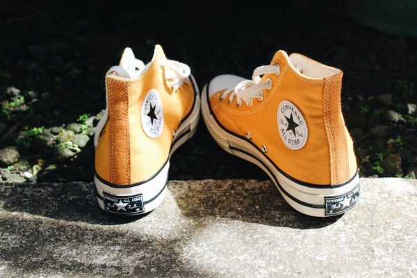 Close-up of orange high top sneakers on sunlit concrete, conveying casual fashion vibes.